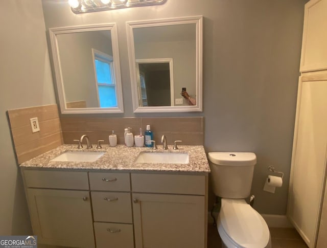 bathroom featuring vanity with extensive cabinet space, toilet, tasteful backsplash, and dual sinks