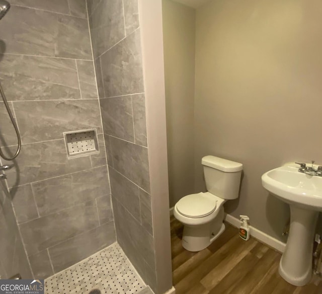 bathroom with a tile shower, sink, toilet, and wood-type flooring