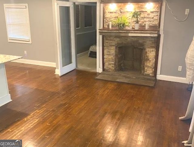 unfurnished living room with a stone fireplace and dark hardwood / wood-style flooring