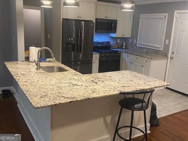 kitchen featuring kitchen peninsula, hardwood / wood-style floors, black appliances, a kitchen bar, and white cabinetry