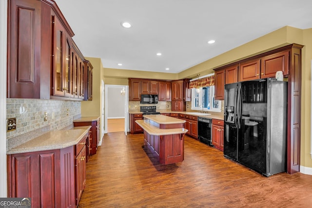 kitchen with light stone countertops, black appliances, a kitchen island, tasteful backsplash, and dark hardwood / wood-style flooring