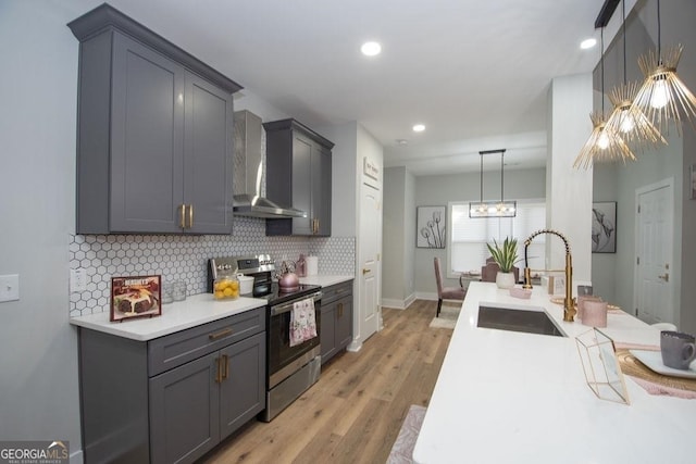 kitchen featuring a notable chandelier, light hardwood / wood-style floors, sink, stainless steel electric range, and wall chimney exhaust hood