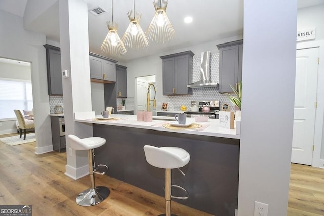 kitchen featuring hanging light fixtures, wall chimney range hood, a breakfast bar, light hardwood / wood-style floors, and stainless steel range with electric stovetop