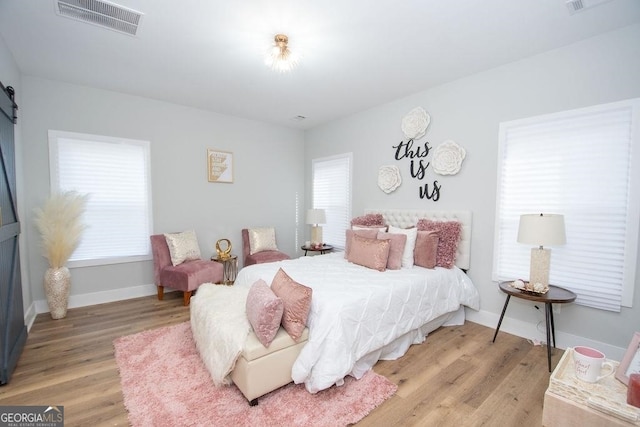 bedroom featuring a barn door, multiple windows, and light hardwood / wood-style flooring