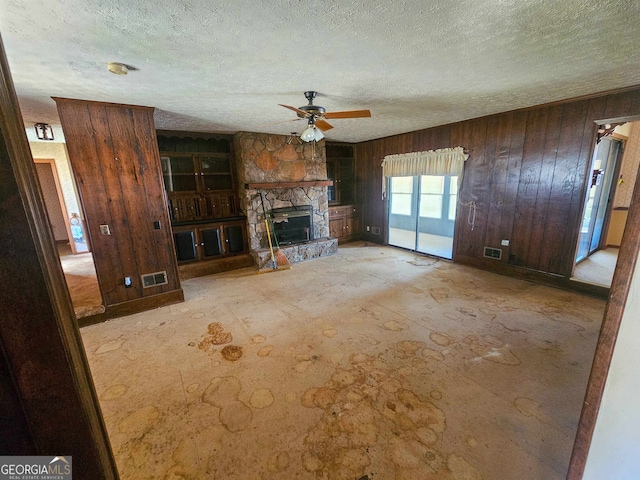 unfurnished living room featuring wood walls, a textured ceiling, ceiling fan, and a fireplace