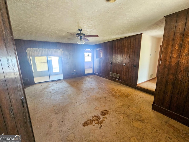 interior space featuring ceiling fan, a textured ceiling, and wooden walls