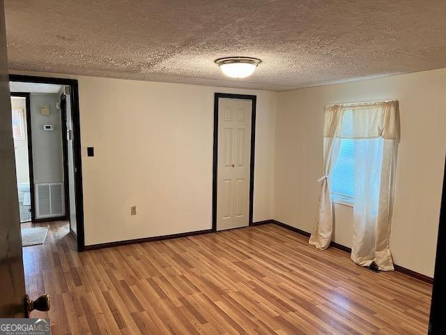 empty room with plenty of natural light, a textured ceiling, and light hardwood / wood-style flooring