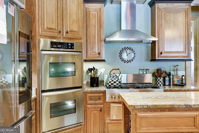 kitchen featuring appliances with stainless steel finishes, wall chimney range hood, and light stone countertops