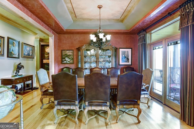 dining space with a raised ceiling, a notable chandelier, and light hardwood / wood-style flooring