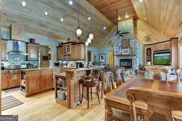 kitchen with wooden ceiling, light wood-type flooring, wall chimney exhaust hood, a stone fireplace, and high vaulted ceiling