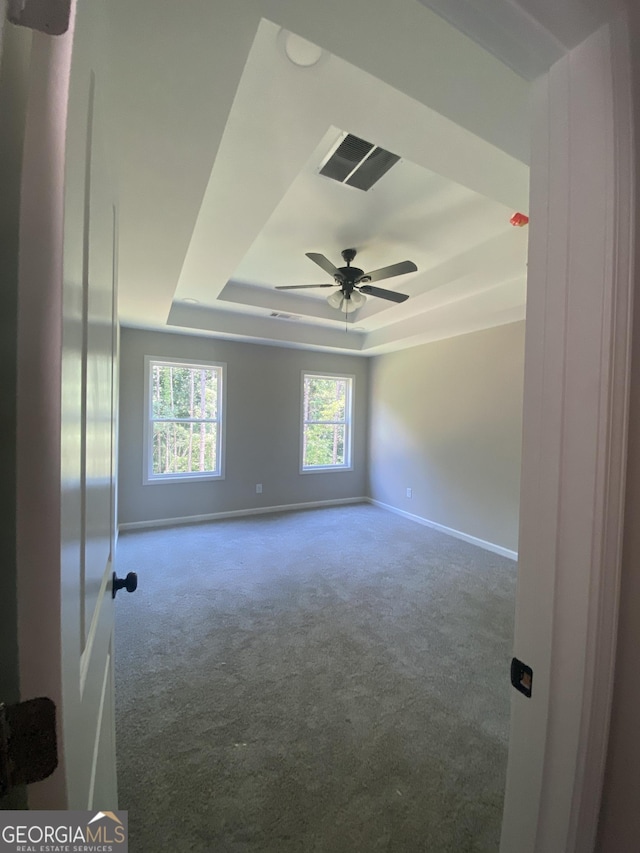 unfurnished room with ceiling fan, carpet, baseboards, and a raised ceiling