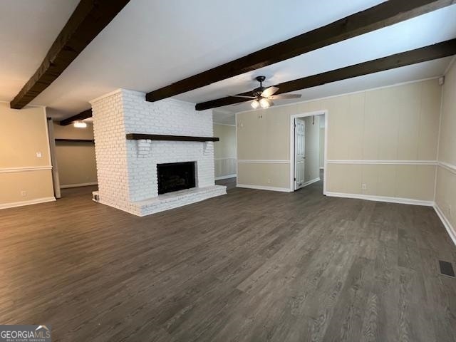 unfurnished living room featuring dark wood-type flooring, beamed ceiling, ceiling fan, a brick fireplace, and brick wall