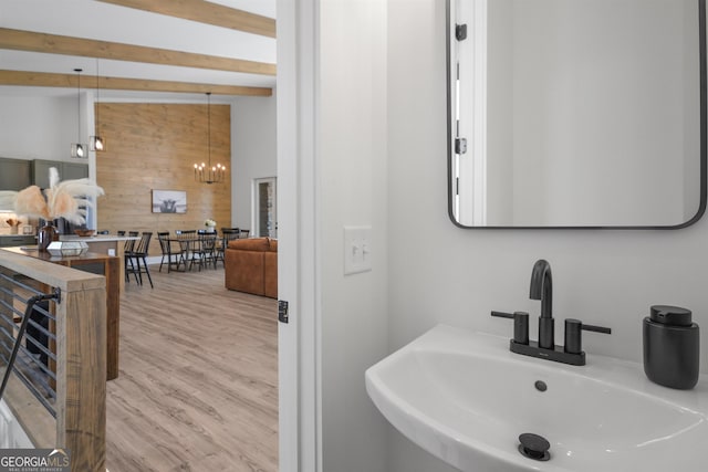 bathroom featuring wood walls, beam ceiling, an inviting chandelier, hardwood / wood-style floors, and sink