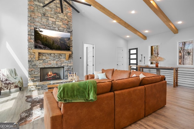 living room featuring ceiling fan, a fireplace, high vaulted ceiling, light hardwood / wood-style floors, and beam ceiling