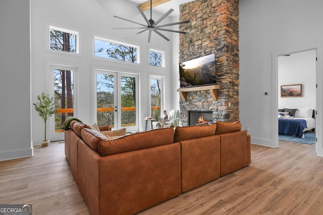 living room with light wood-type flooring, beamed ceiling, ceiling fan, a fireplace, and a high ceiling