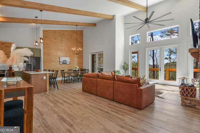 living room with wood walls, light hardwood / wood-style floors, french doors, high vaulted ceiling, and ceiling fan with notable chandelier