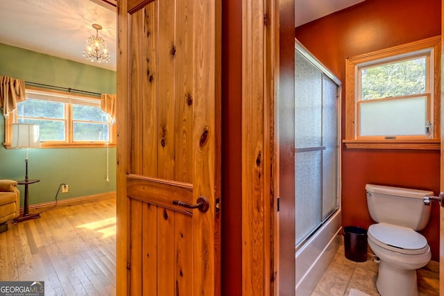 bathroom with a chandelier, hardwood / wood-style floors, shower / bath combination with glass door, and toilet