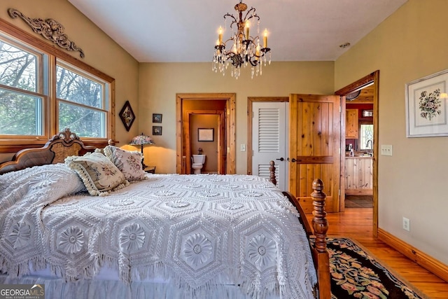 bedroom with ensuite bath, a notable chandelier, and hardwood / wood-style floors