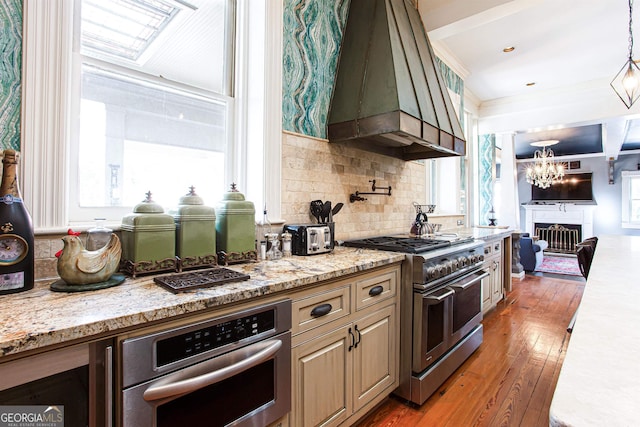 kitchen with stainless steel appliances, a notable chandelier, premium range hood, hardwood / wood-style floors, and tasteful backsplash