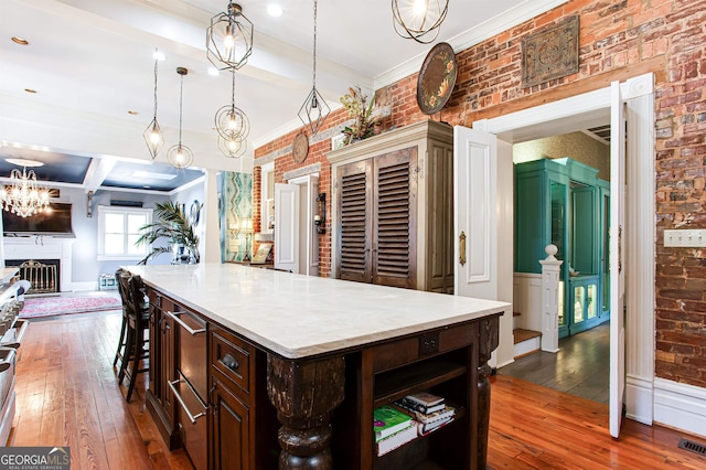 kitchen with dark hardwood / wood-style flooring, dark brown cabinetry, brick wall, a center island, and pendant lighting