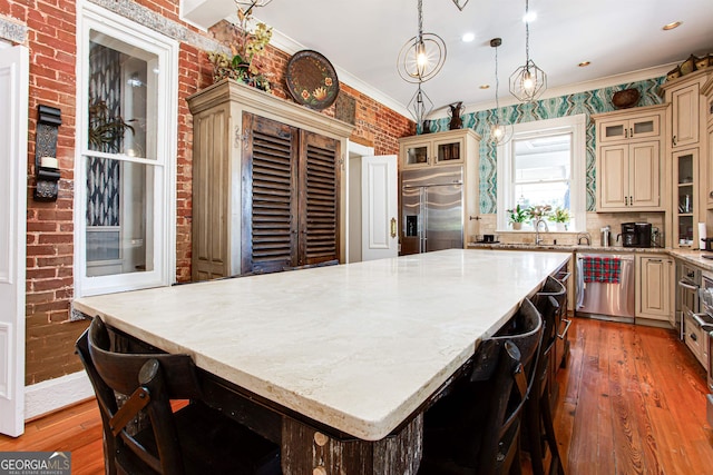 kitchen featuring appliances with stainless steel finishes, a center island, wood-type flooring, decorative light fixtures, and ornamental molding