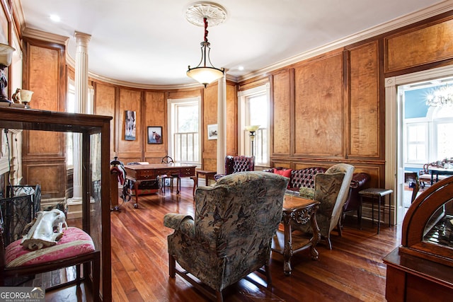 living room featuring wooden walls, crown molding, ornate columns, and dark wood-type flooring