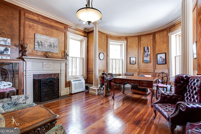 home office featuring dark wood-type flooring, wooden walls, a fireplace, ornamental molding, and ornate columns