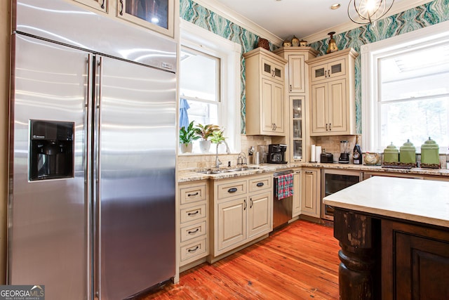 kitchen featuring appliances with stainless steel finishes, light hardwood / wood-style floors, crown molding, backsplash, and cream cabinets