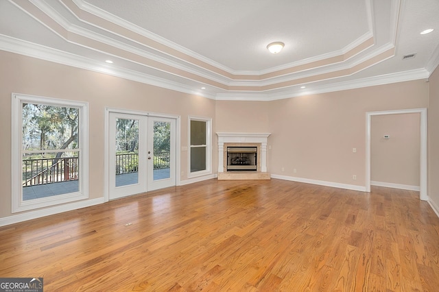 unfurnished living room with light wood-type flooring, a fireplace, crown molding, a tray ceiling, and french doors