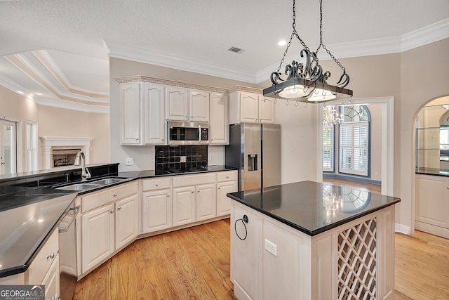 kitchen featuring pendant lighting, sink, ornamental molding, stainless steel appliances, and light wood-type flooring