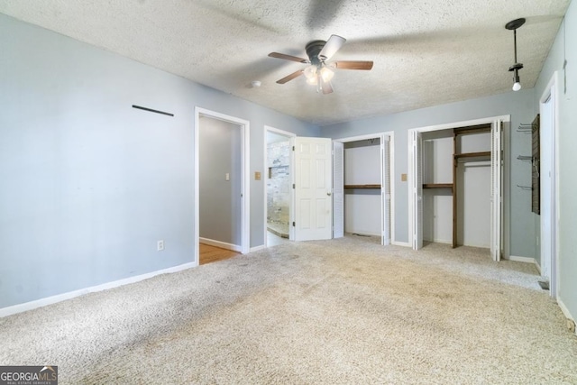 unfurnished bedroom with light carpet, a textured ceiling, ceiling fan, and multiple closets