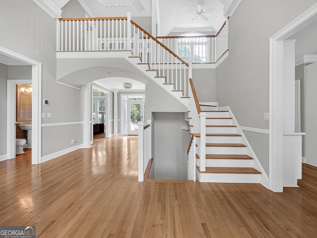 stairs featuring ornamental molding, a high ceiling, light wood-type flooring, and ceiling fan with notable chandelier