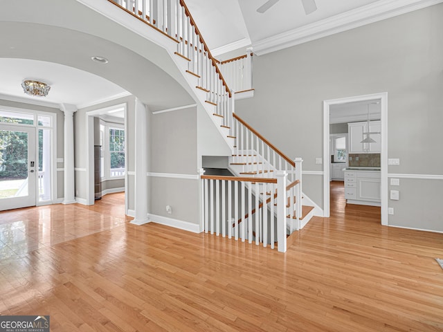 staircase featuring ornamental molding, ceiling fan, a towering ceiling, and light wood-type flooring