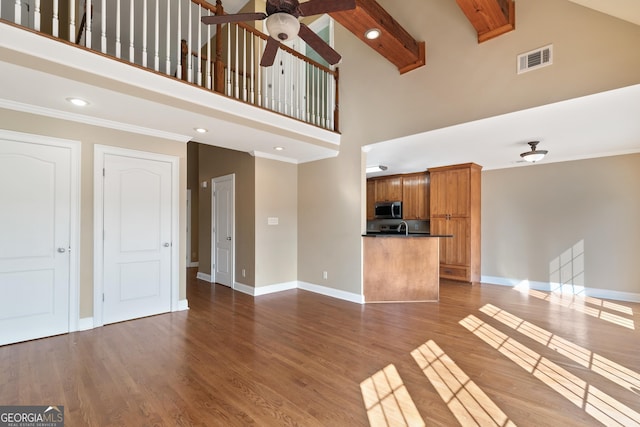 unfurnished living room featuring ceiling fan, light wood-type flooring, ornamental molding, and a high ceiling