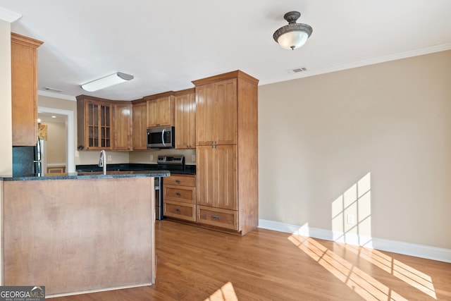 kitchen featuring ornamental molding, dark stone countertops, stainless steel appliances, and light wood-type flooring