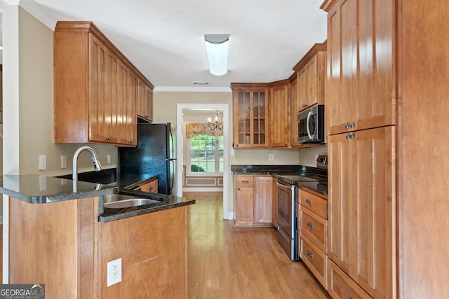 kitchen with dark stone countertops, appliances with stainless steel finishes, sink, a notable chandelier, and light wood-type flooring