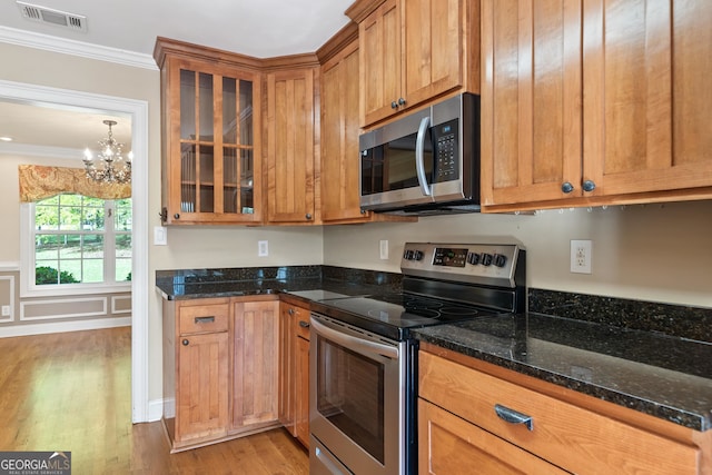 kitchen with dark stone counters, stainless steel appliances, a chandelier, light hardwood / wood-style flooring, and ornamental molding