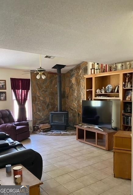 living room featuring ceiling fan, a textured ceiling, a wood stove, and light tile floors