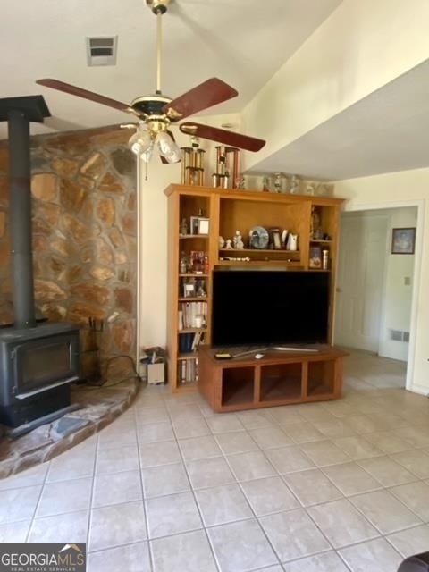 unfurnished living room featuring ceiling fan, lofted ceiling, light tile floors, and a wood stove