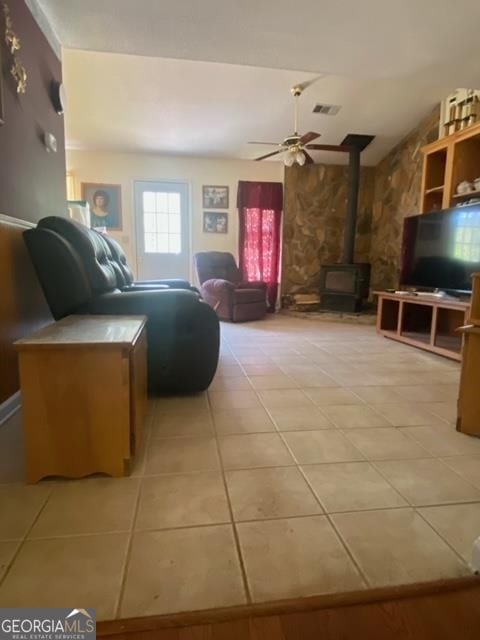 living room with a wood stove, ceiling fan, and light tile flooring