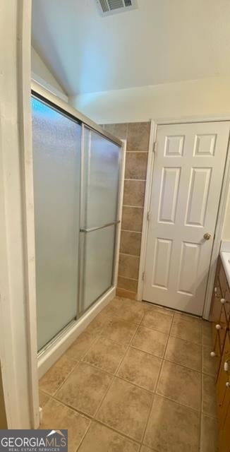 bathroom with a shower with door, tile flooring, vanity, and vaulted ceiling