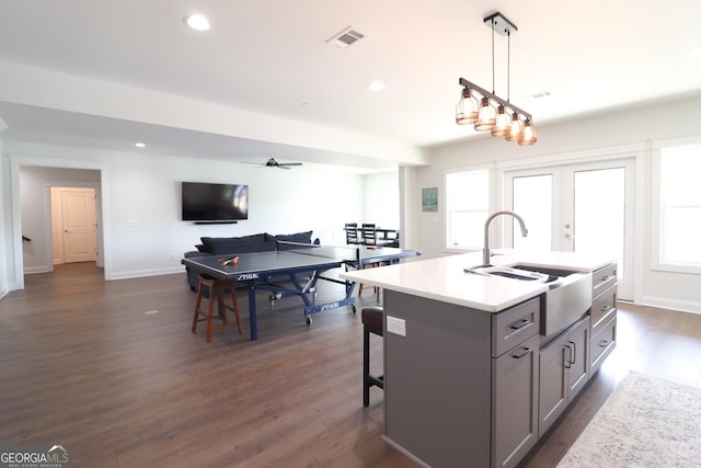 kitchen with gray cabinetry, pendant lighting, dark wood-type flooring, and a kitchen island with sink