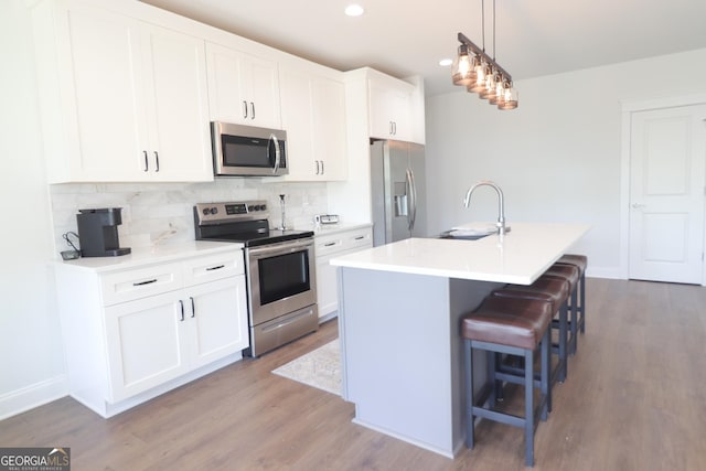 kitchen with appliances with stainless steel finishes, a center island with sink, white cabinets, and a kitchen bar