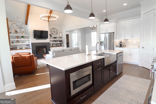 kitchen with appliances with stainless steel finishes, vaulted ceiling with beams, white cabinetry, hanging light fixtures, and wood-type flooring