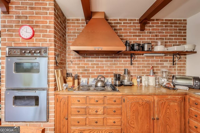 kitchen with beam ceiling, multiple ovens, stovetop, and ventilation hood