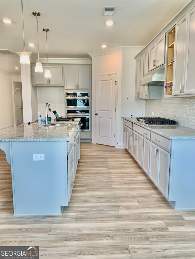 kitchen featuring hanging light fixtures, appliances with stainless steel finishes, light hardwood / wood-style floors, and light stone counters