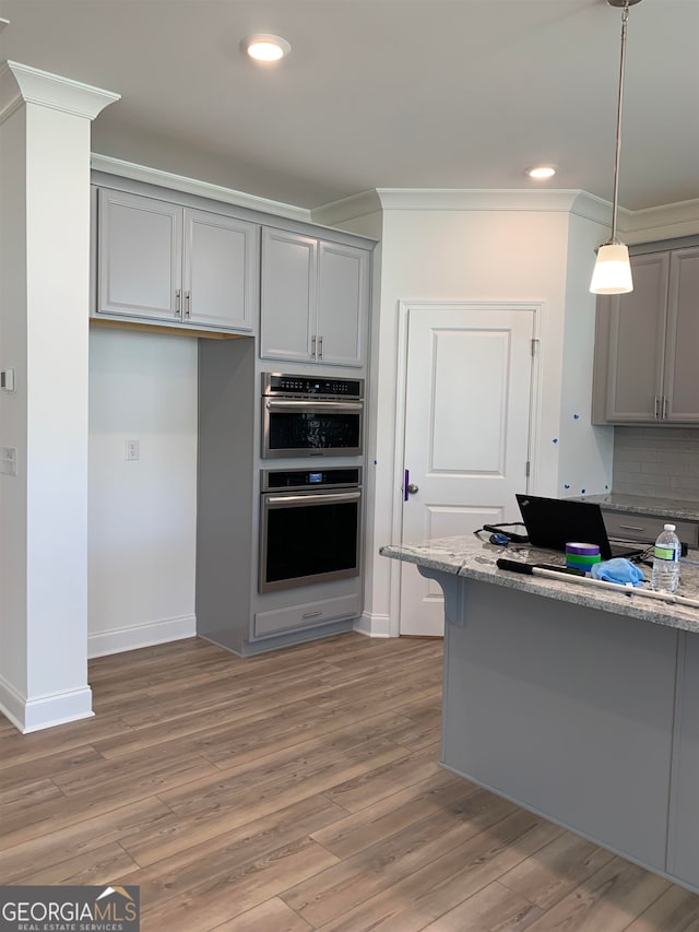 kitchen with stainless steel double oven, light hardwood / wood-style floors, tasteful backsplash, and light stone countertops