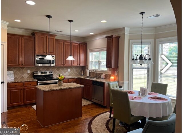 kitchen with decorative light fixtures, a kitchen island, stainless steel appliances, and light stone countertops