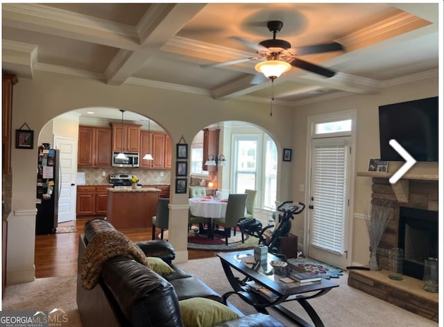 living room featuring ceiling fan, coffered ceiling, beamed ceiling, a fireplace, and ornamental molding