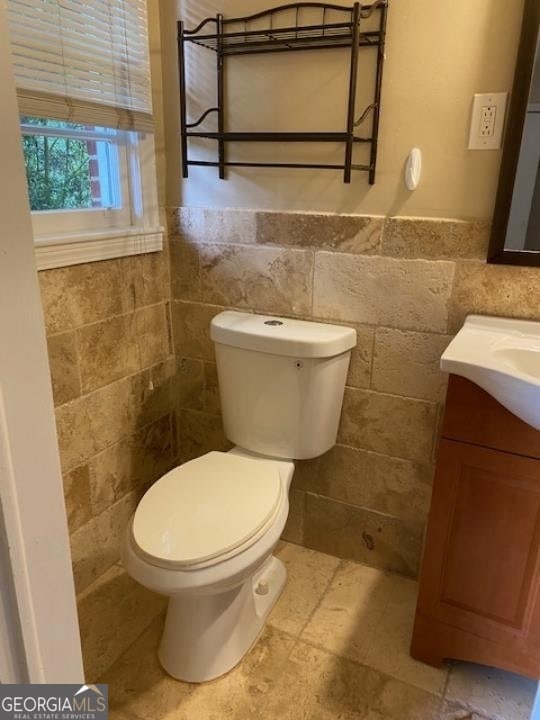 bathroom with tile floors, tile walls, vanity, and toilet